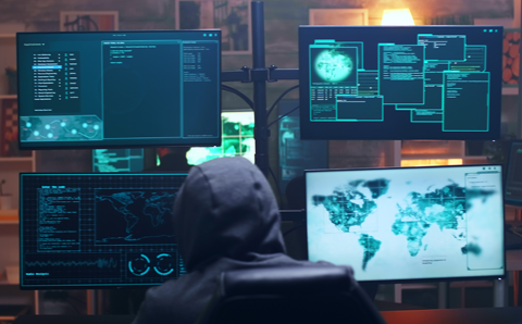Person in a hoodie sitting in front of multiple monitors.