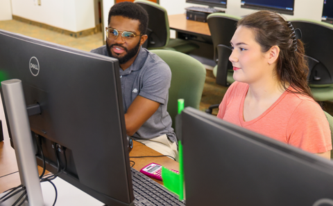 A male and female student looking at a computer monitor.