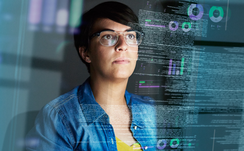 A woman looking at a see-through screen with different graphs and data on it.